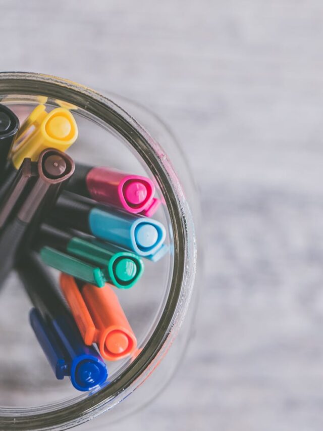 A flat lay image showcasing colorful pens arranged in a mason jar on a light wooden desk.